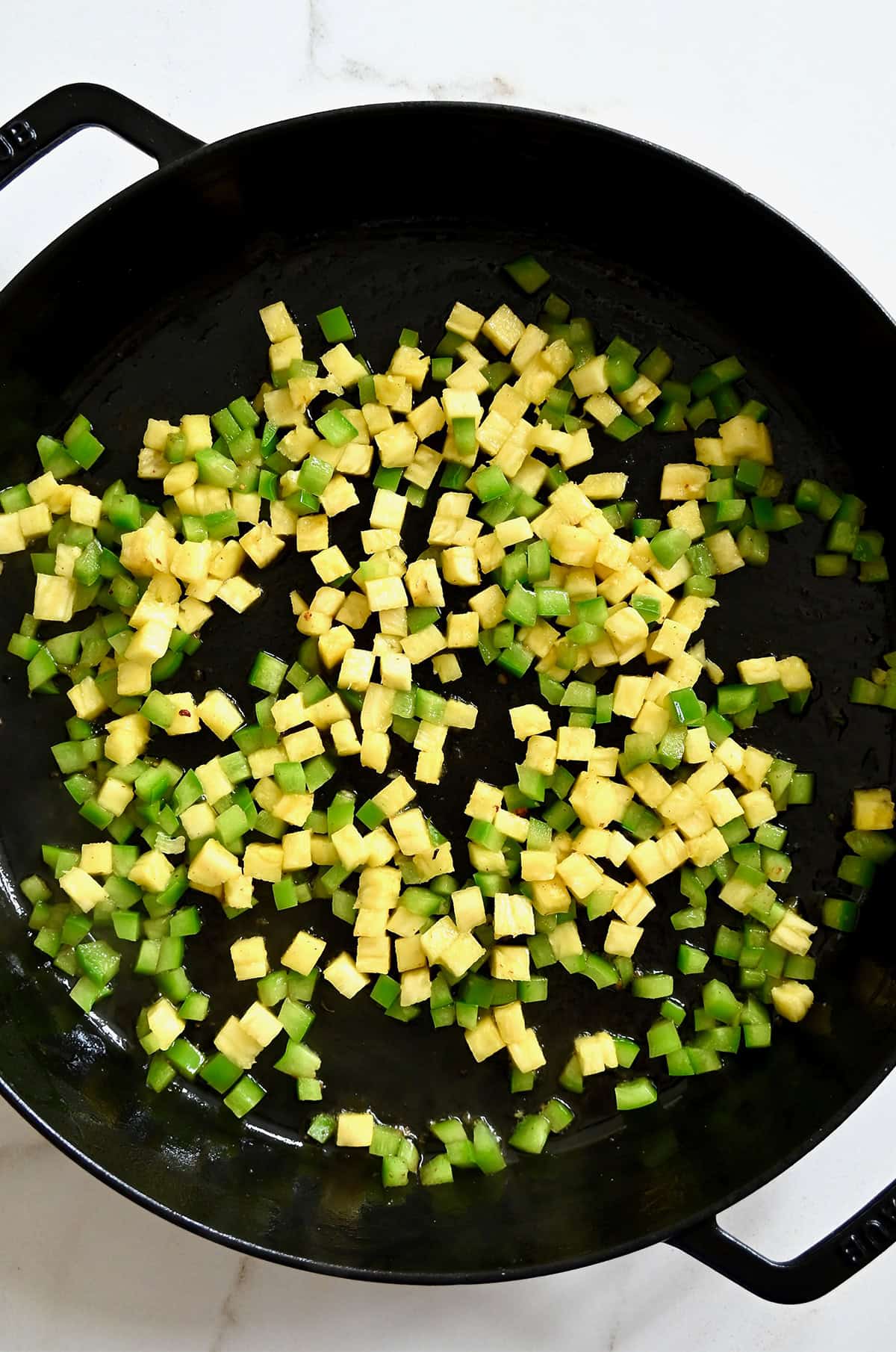 Diced pineapple and green peppers cooking in a large skillet.