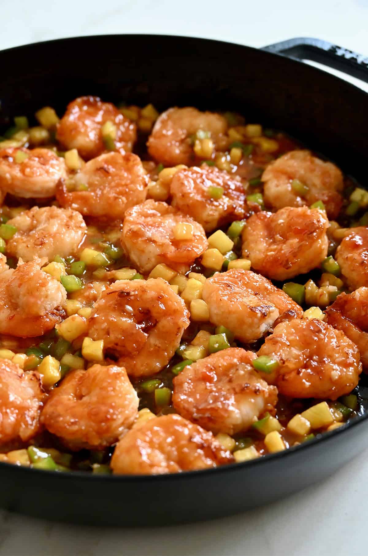 Crispy pineapple shrimp with diced green bell pepper and pineapple in a skillet.