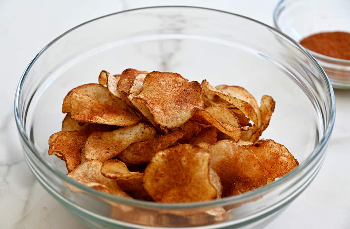 Homemade chips being tossed with seasoning in a clear bowl