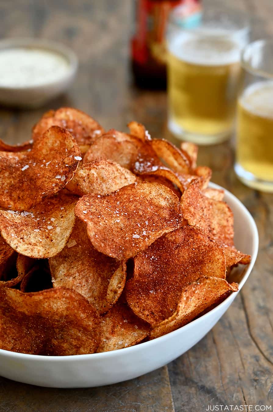 A white serving bowl containing Homemade Barbecue Potato Chips with two glasses filled with beer in the background