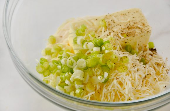 A glass bowl containing butter, mayo, cheese and scallions