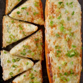 A baking sheet containing a loaf of garlic bread cut into triangles