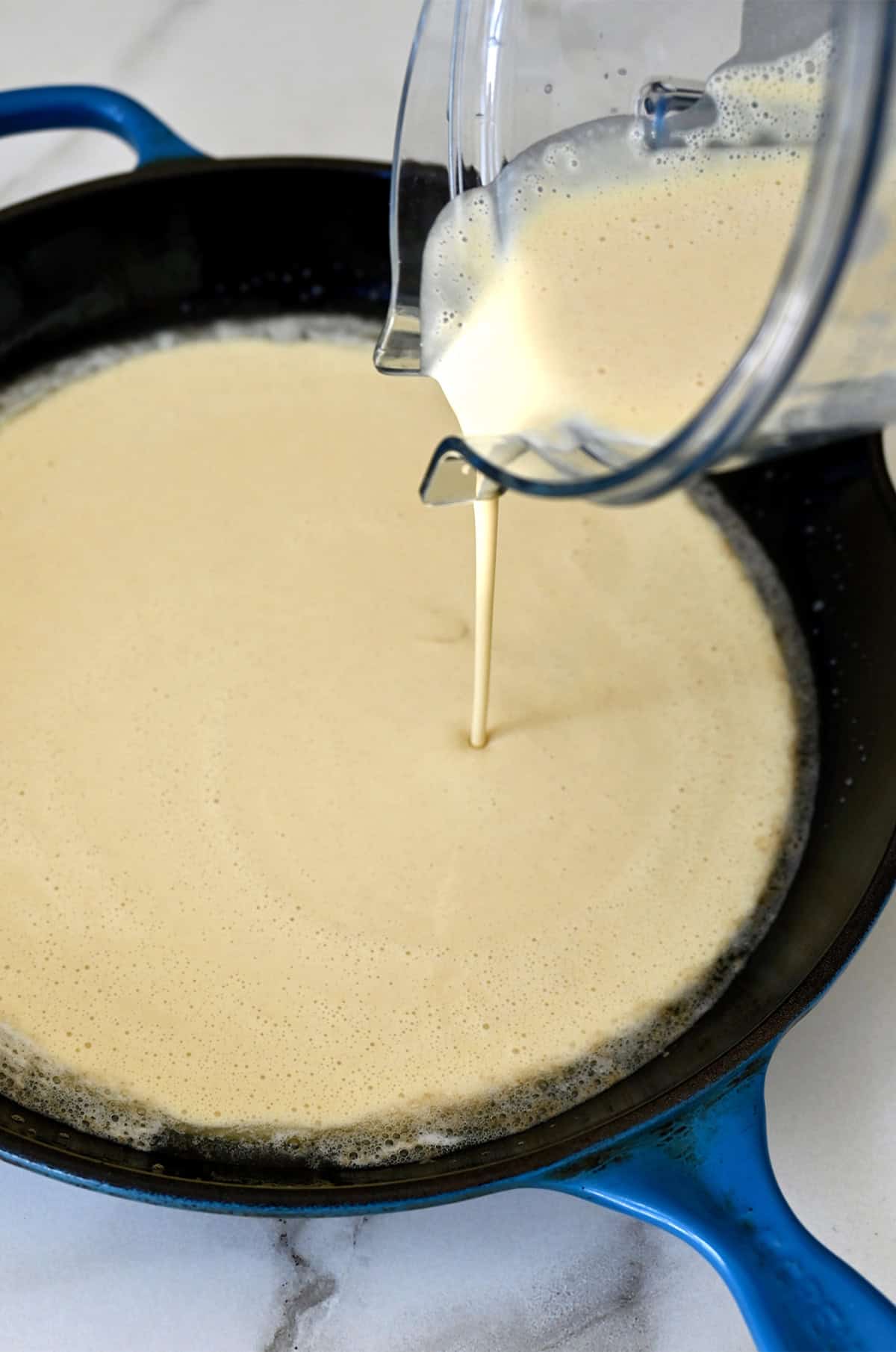 German pancake batter being poured from a blender into a cast iron skillet that's been coated with melted butter.