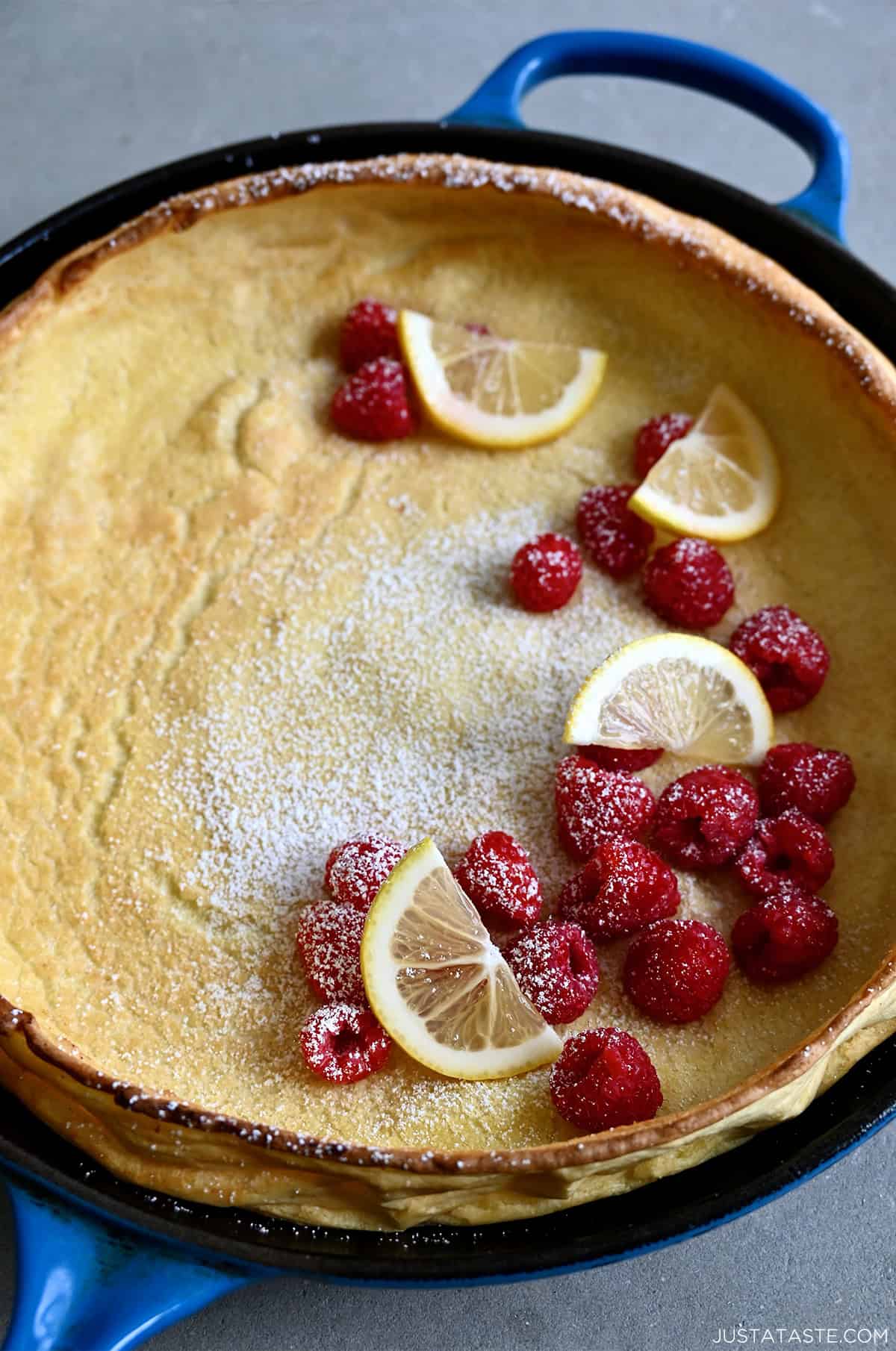 A Dutch baby pancake dusted with powdered sugar and topped with fresh raspberries and slices of lemon. 