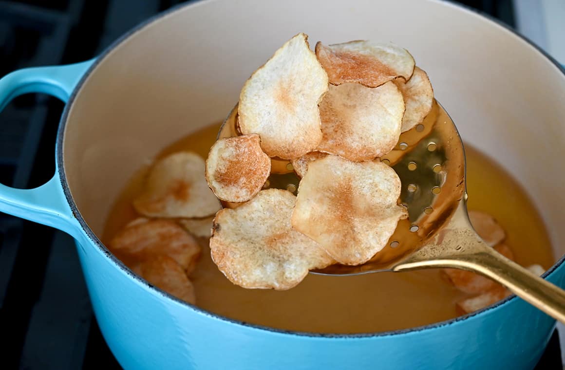 A slotted spoon with freshly fried potato chips over a large stockpot containing oil