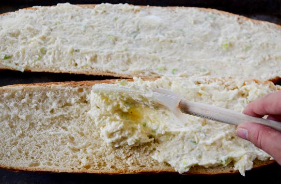 A loaf of bread being slathered with garlic butter