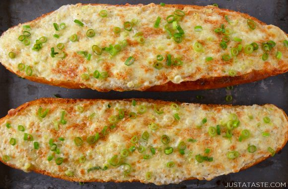 Two loafs of garlic bread on a baking sheet topped with sliced scallions