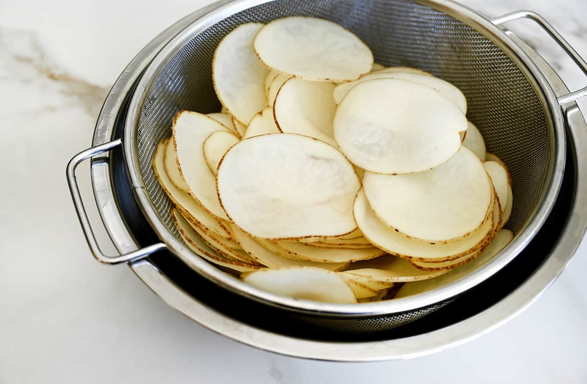 Thin slices of potato soaking in an ice water bath