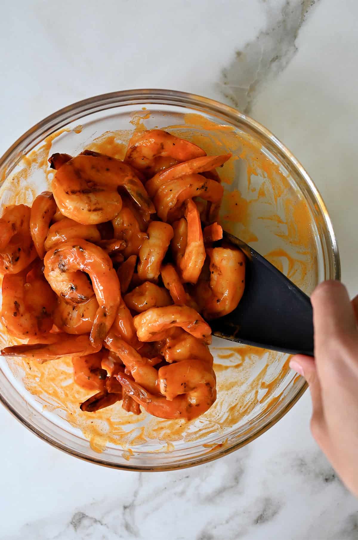 Cooked shrimp being tossed in homemade Buffalo sauce in a glass bowl.
