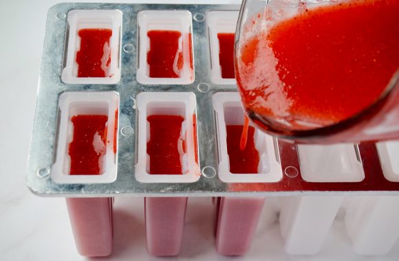 Strawberry margarita mixture being poured into popsicle molds