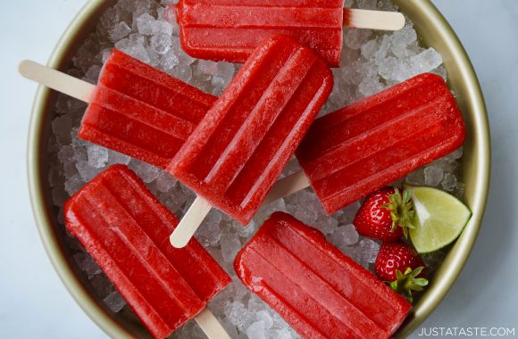 Easy strawberry margarita popsicles over ice next to lime wedge and fresh strawberries