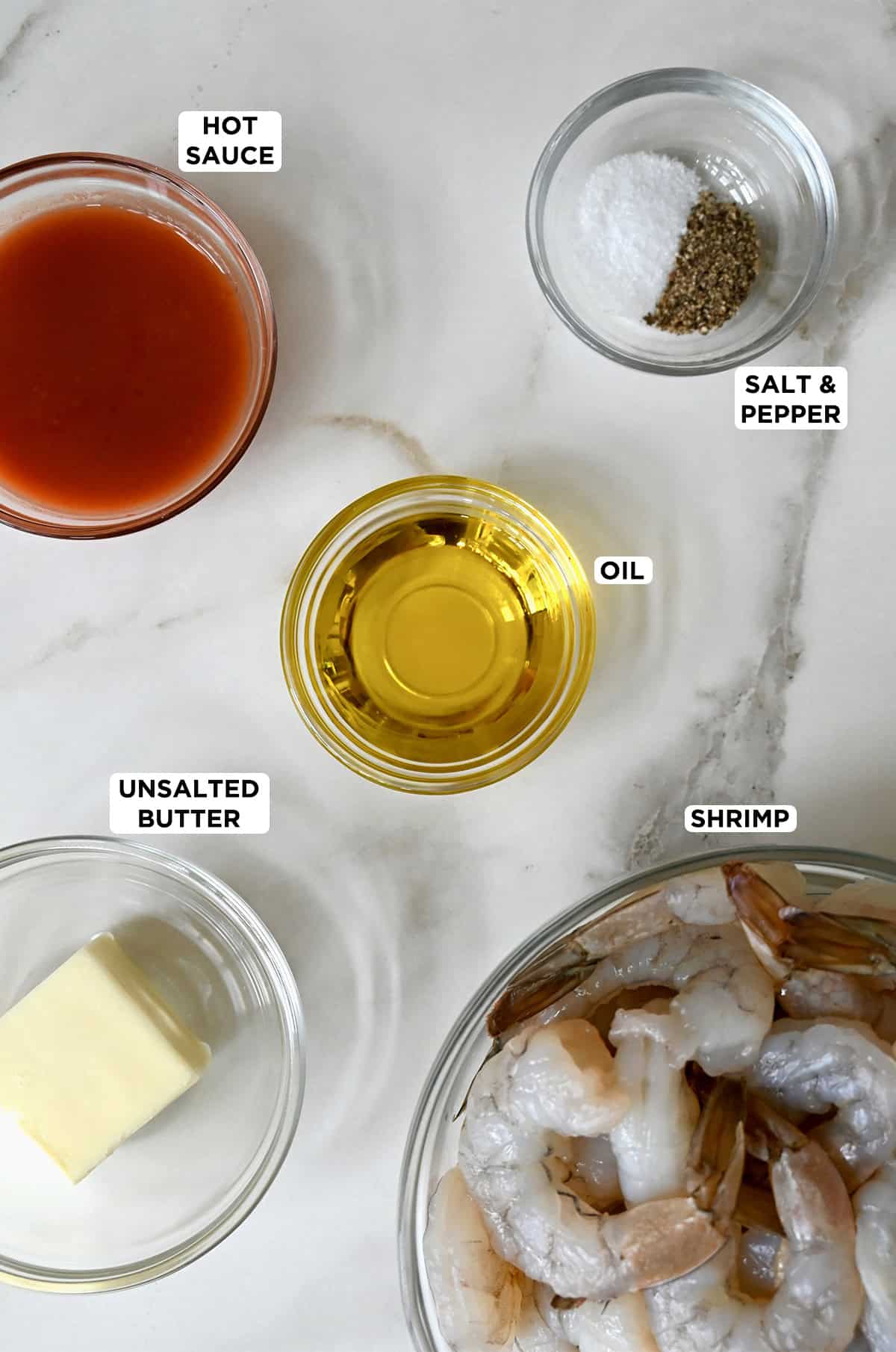 Glass bowls containing hot sauce, salt and pepper, olive oil, raw shrimp and unsalted butter.