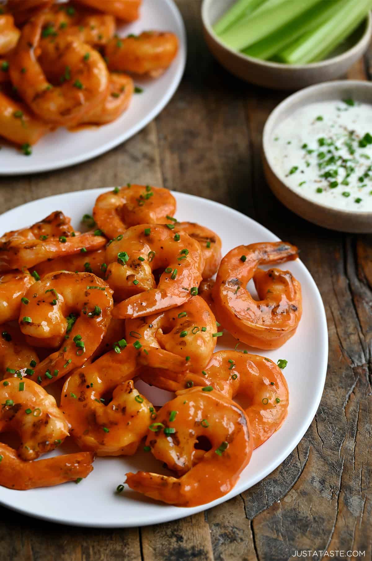Buffalo shrimp piled on a white plate next to a small bowl filled with blue cheese dressing.