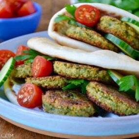 Easy Homemade Falafel tucked inside pita bread with Tahini Sauce, cucumbers, tomatoes and parsley. Small blue blue with cherry tomatoes in background.