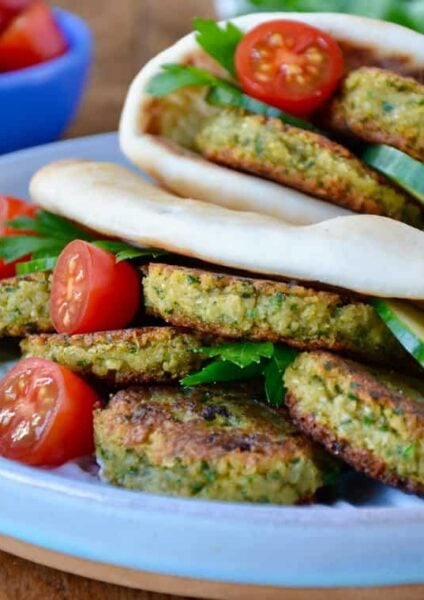 Easy Homemade Falafel tucked inside pita bread with Tahini Sauce, cucumbers, tomatoes and parsley. Small blue blue with cherry tomatoes in background.