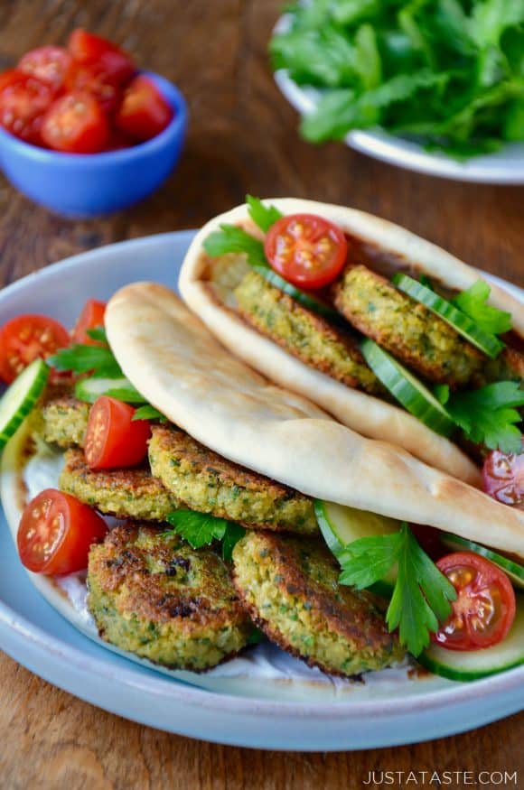 Easy Homemade Falafel tucked inside pita bread with Tahini Sauce, cucumbers, tomatoes and parsley. Small blue blue with cherry tomatoes and white plate with chopped parsley in background.