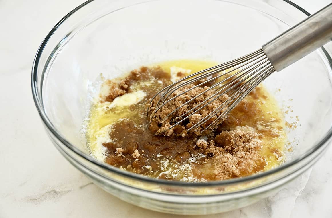 A whisk in a clear bowl with melted butter and brown sugar.