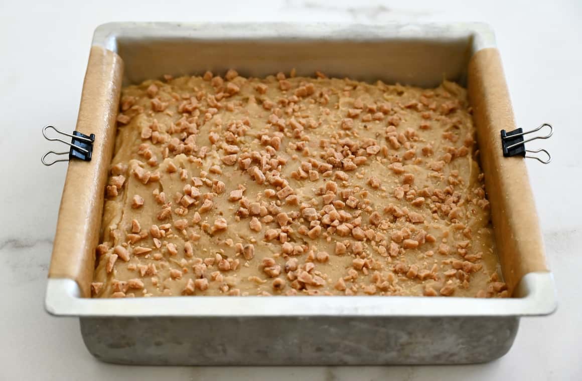 A parchment paper-lined baking pan secured with metal clips containing blondie batter.