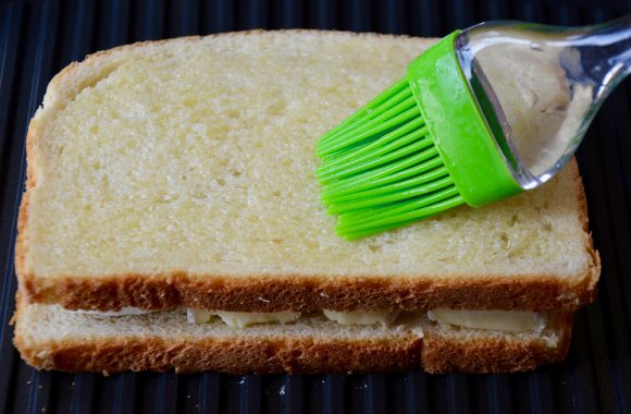 A chocolate and brie sandwich on a panini maker being brushed with melted butter