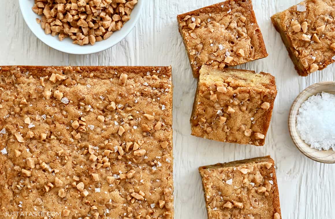 A top-down view of sliced toffee blondies next to a small bowl containing sea salt and another small bowl containing toffee bits.