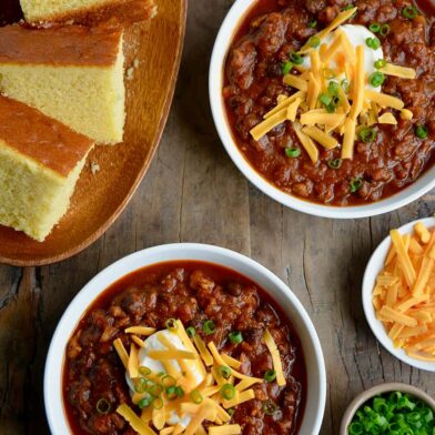 Two white bowls containing pumpkin turkey chili with a plate of cornbread