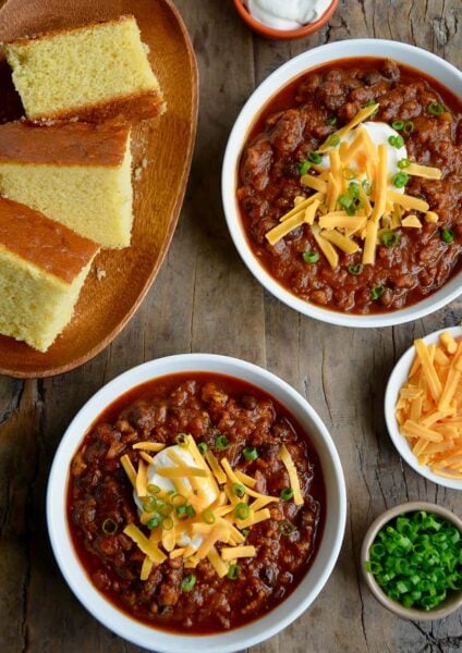 Two white bowls containing pumpkin turkey chili with a plate of cornbread