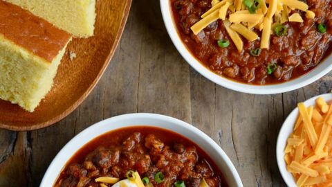 Two white bowls containing pumpkin turkey chili with a plate of cornbread