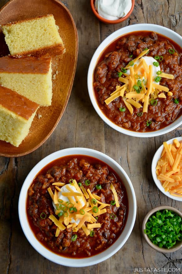 Two white bowls containing pumpkin turkey chili with a plate of cornbread