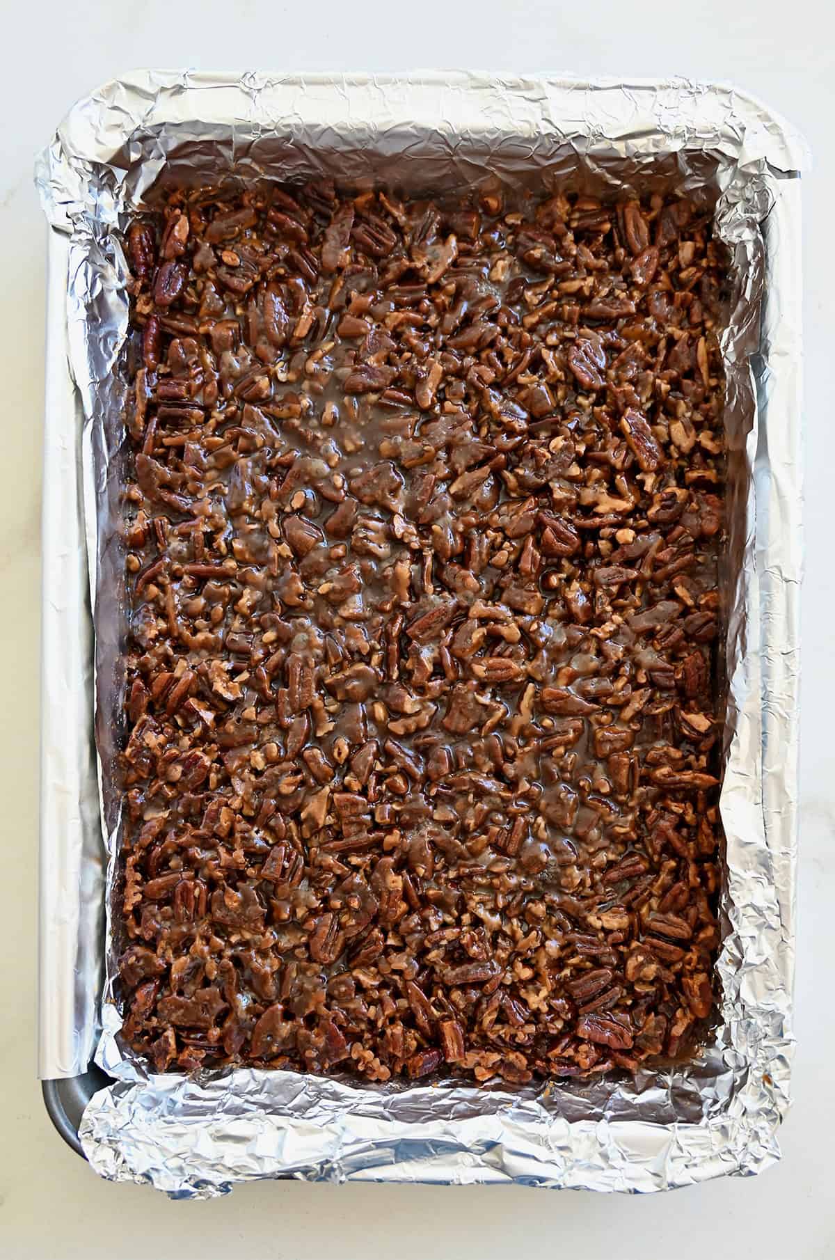 Freshly baked pecan pie bars in an aluminum foil-lined baking pan, ready to be lifted out for slicing.