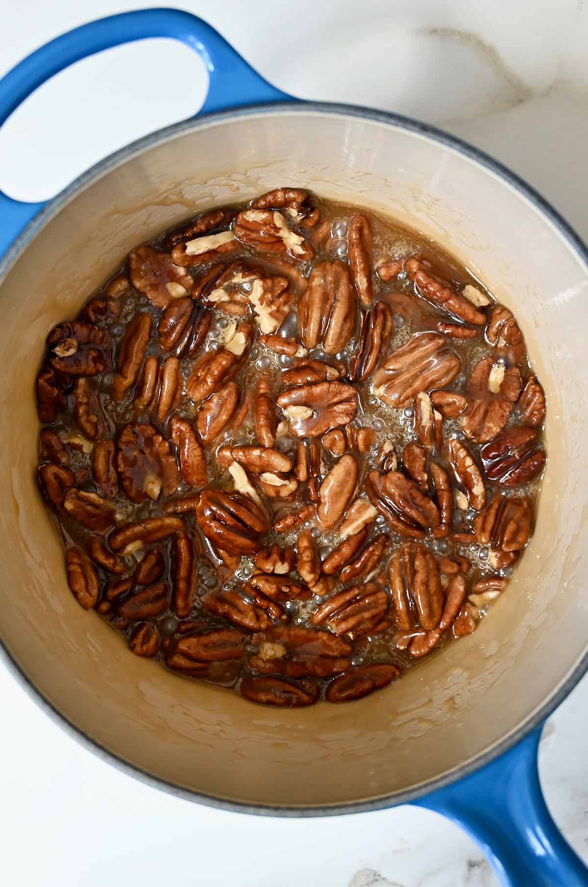 A saucepan containing halved pecans in a caramel-like mixture.
