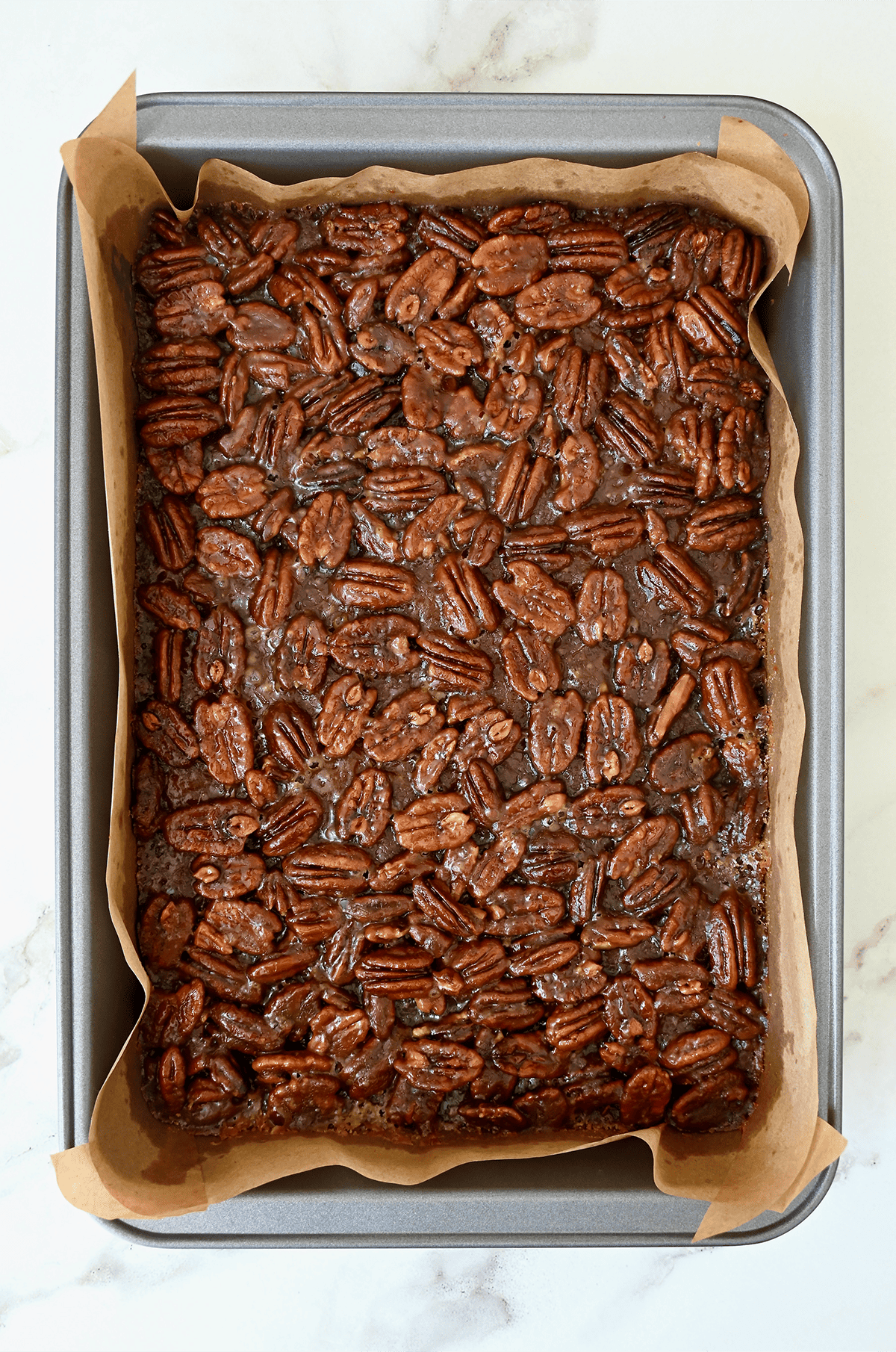 Freshly baked pecan pie bars in a parchment paper-lined baking pan.