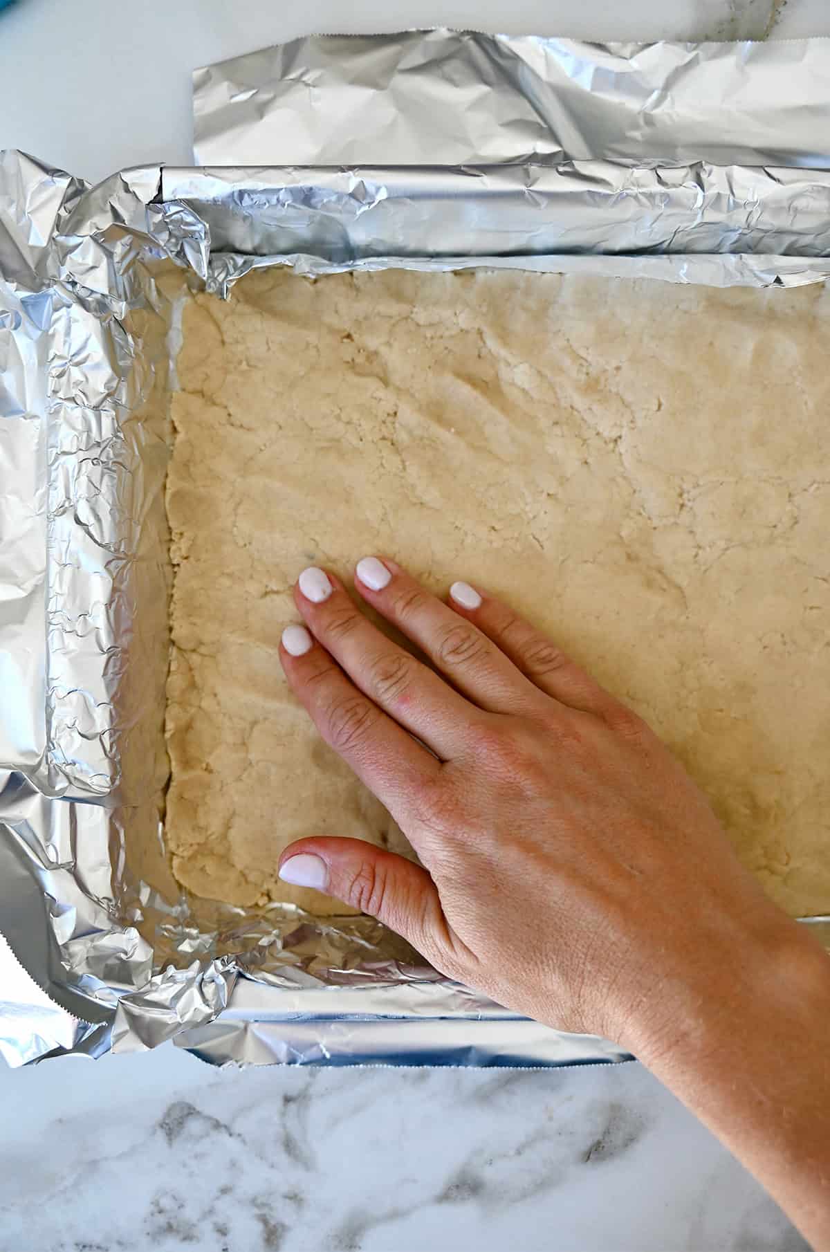 Pressing shortbread dough into a tinfoil-lined baking pan.