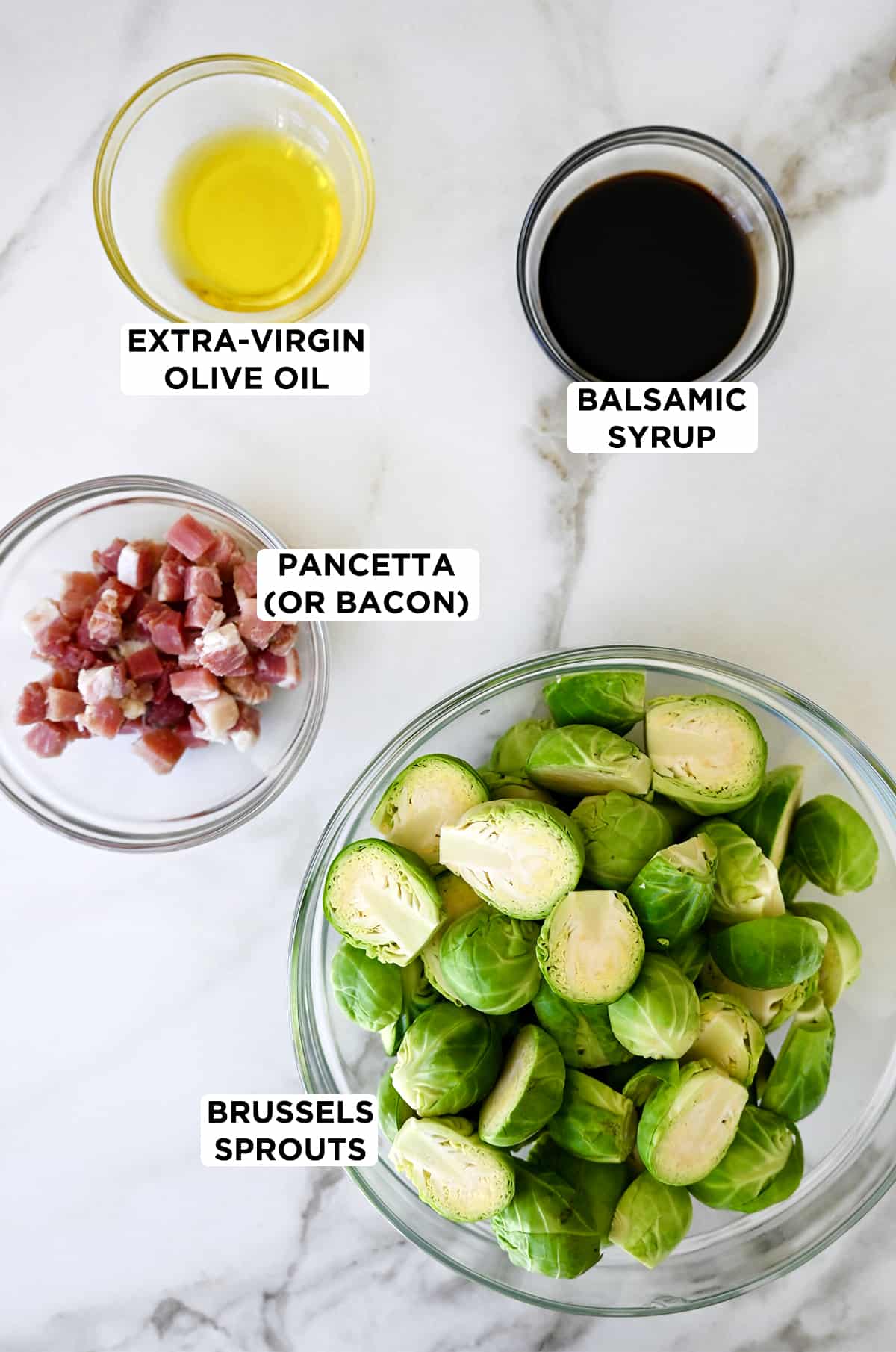 Various sizes of clear bowls containing extra-virgin olive oil, balsamic syrup, Brussels sprouts and chopped pancetta.