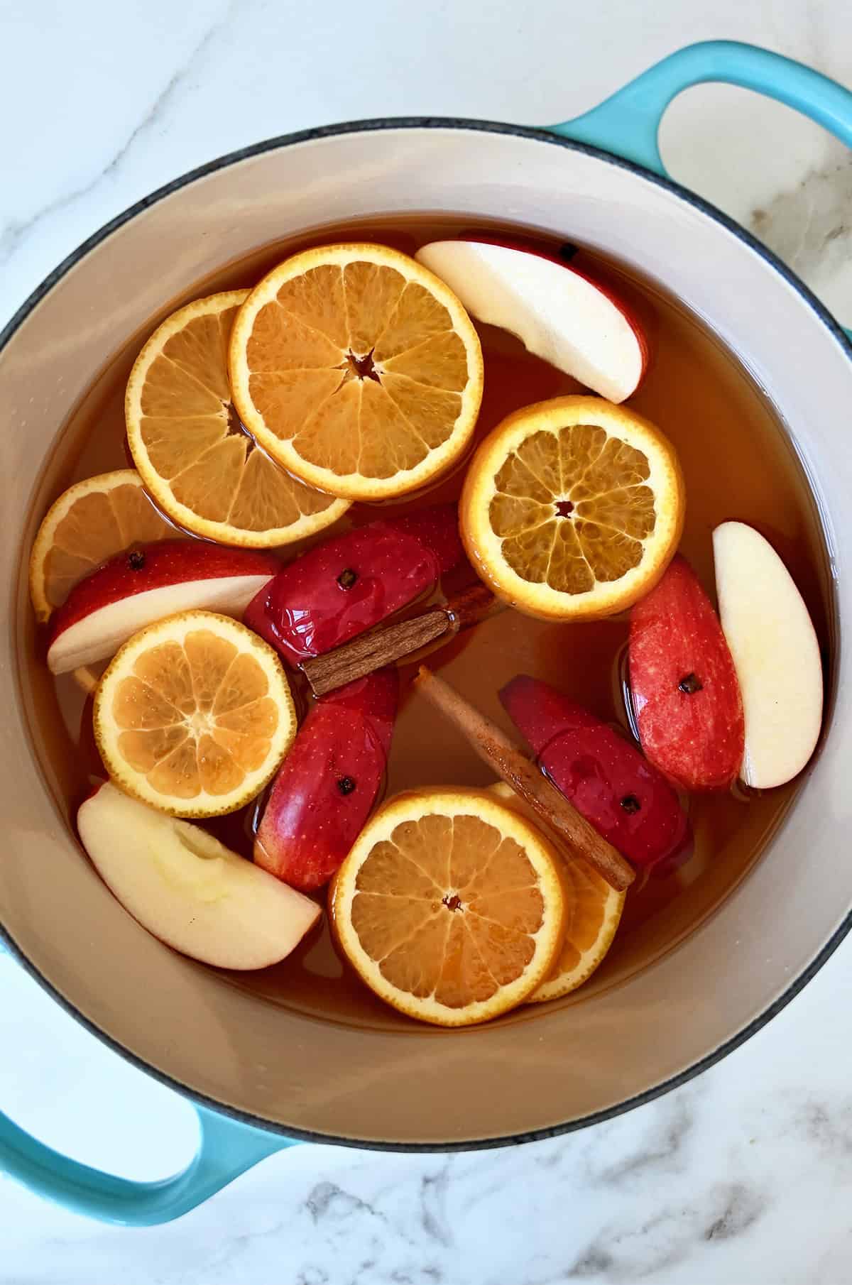 Mulled cider with cinnamon sticks, orange slices and apple wedges in a large pot.