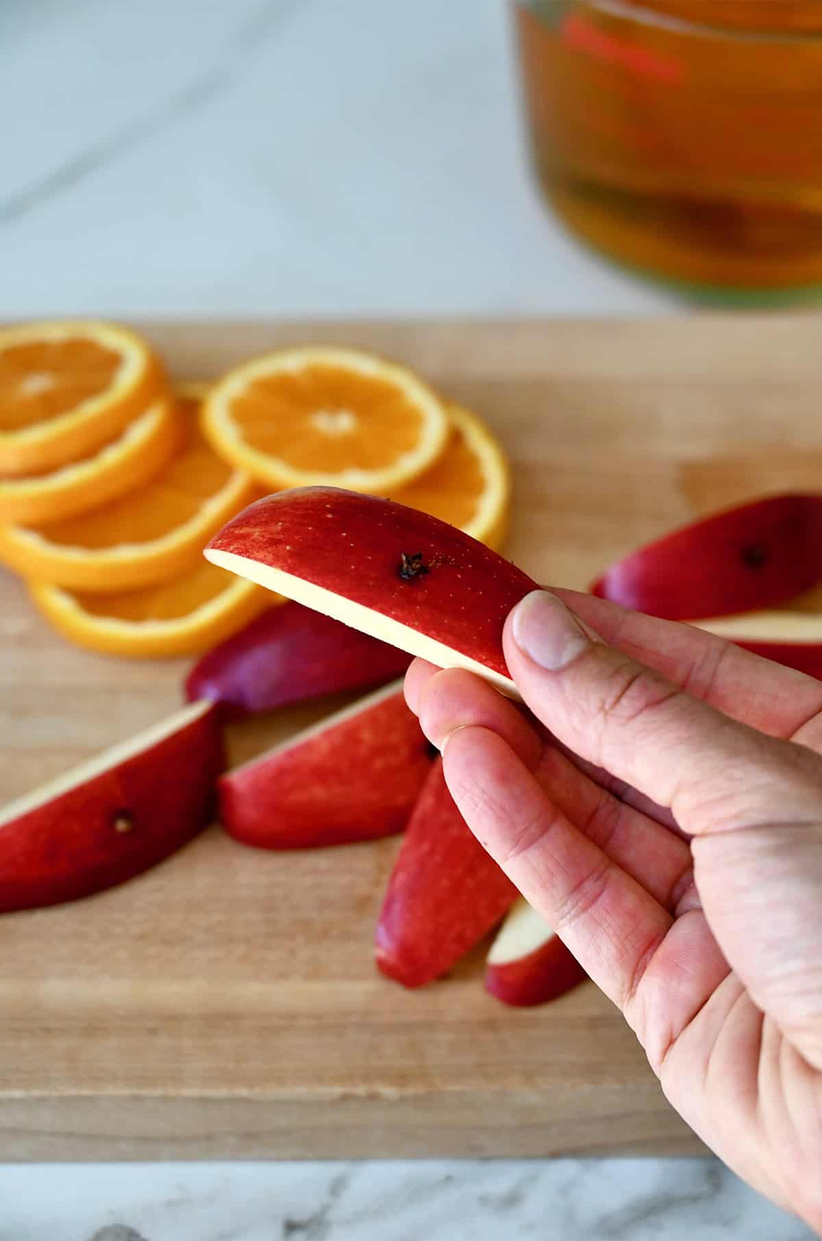 A hand holds an apple wedge with a clove pierced through the skin.