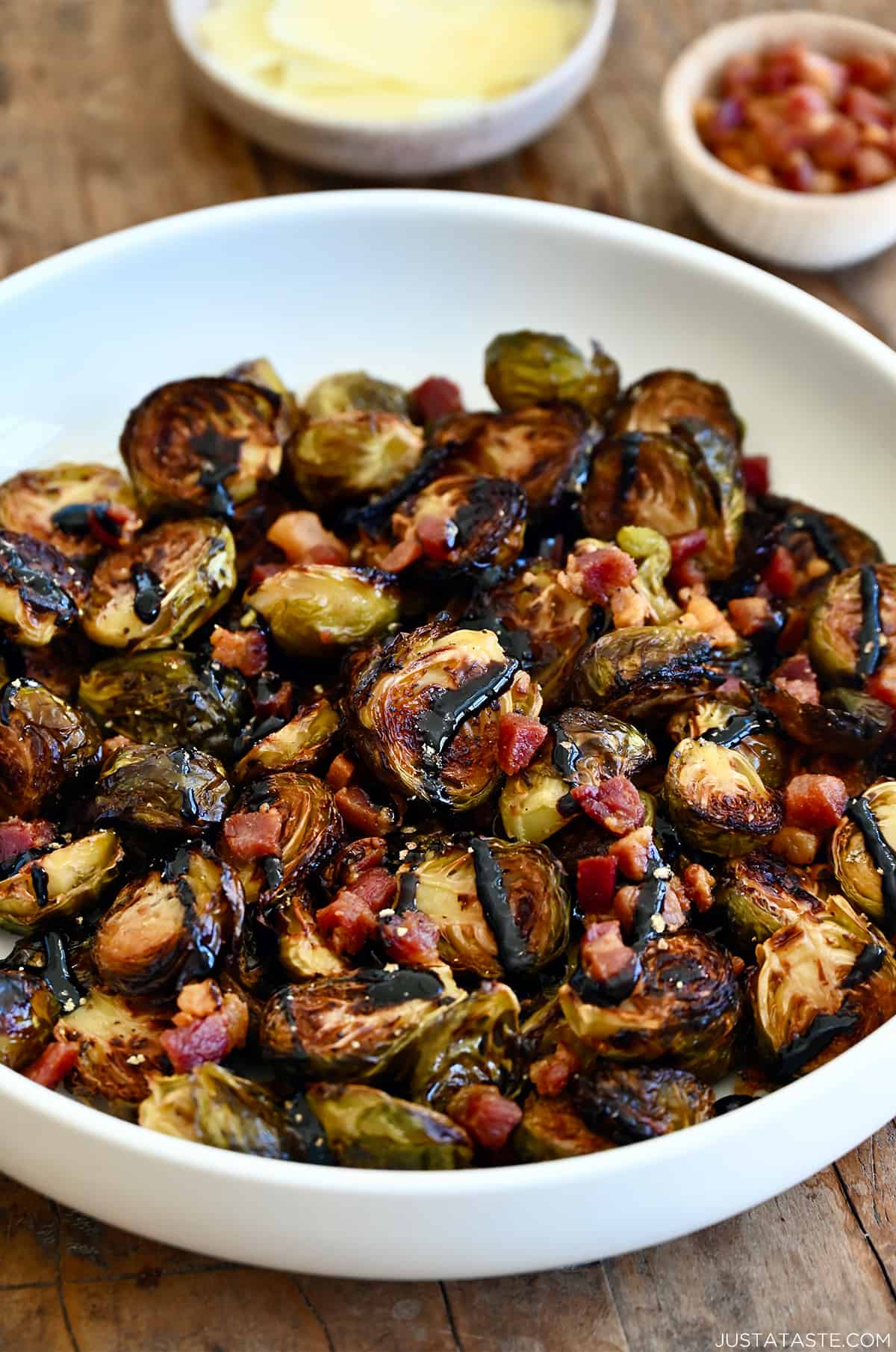 Roasted Brussels sprouts with pancetta bits all drizzled with thick balsamic syrup in a white serving bowl.