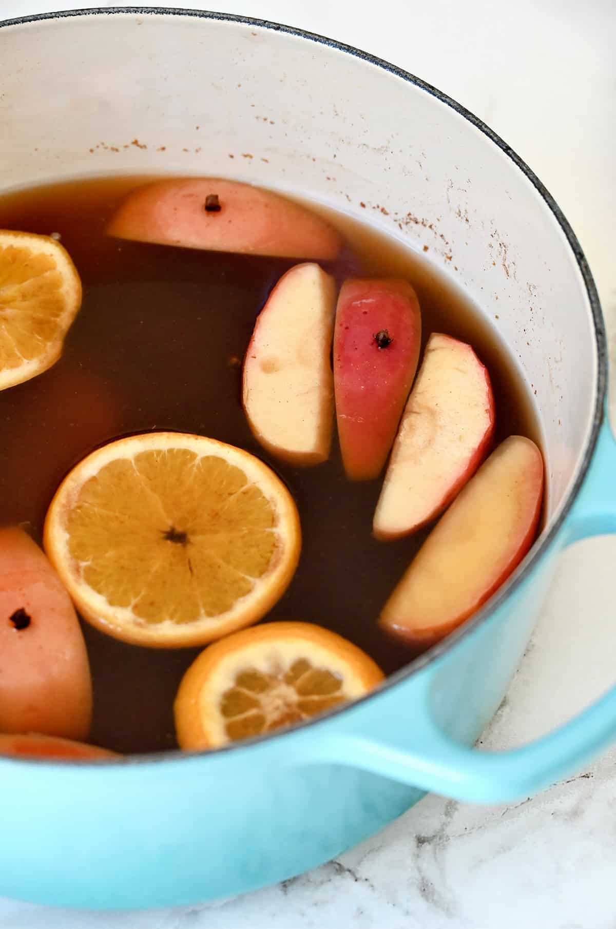 Simmered mulled cider with orange slices and apple wedges in a pot.