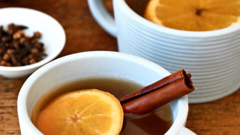 Two mugs containing spiked apple cider with an orange slice and a cinnamon stick.