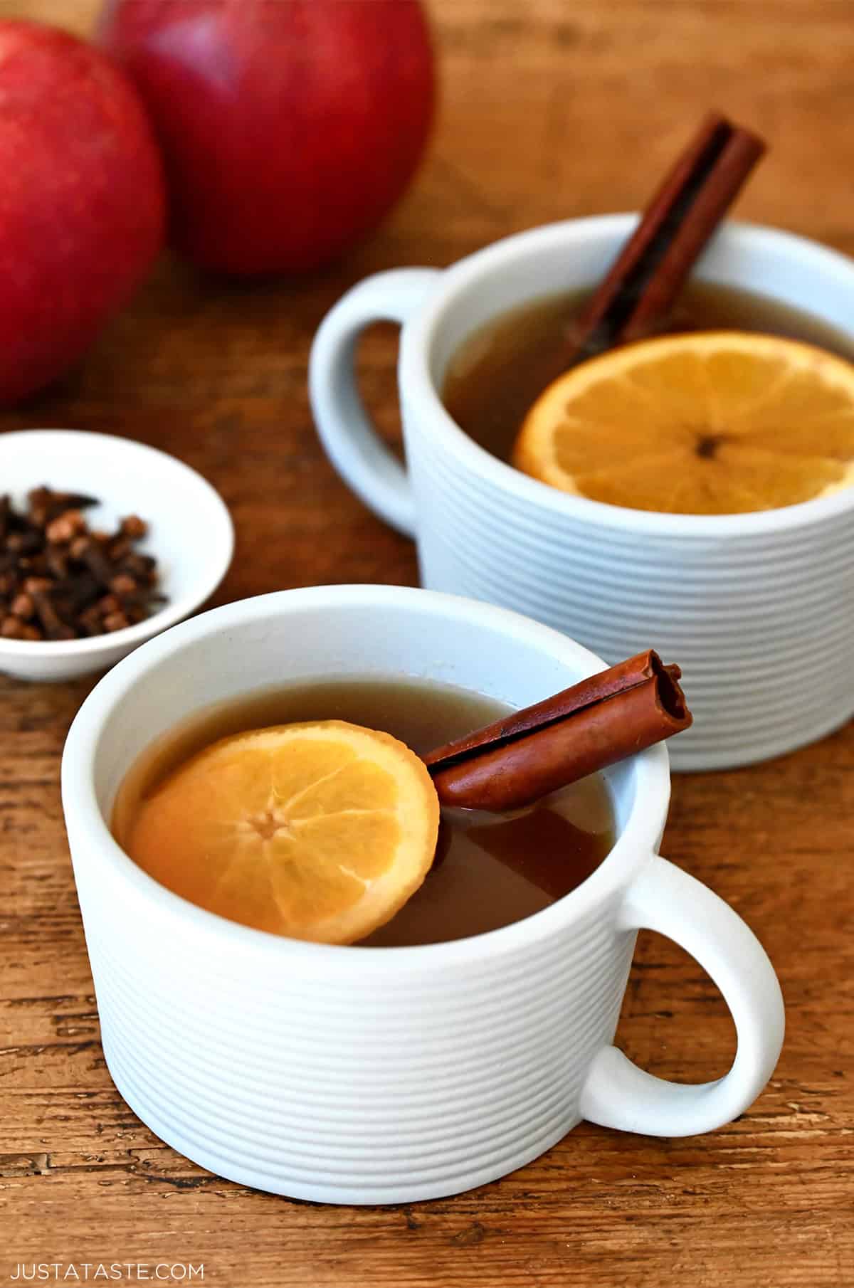 Two mugs containing spiked apple cider with an orange slice and a cinnamon stick.