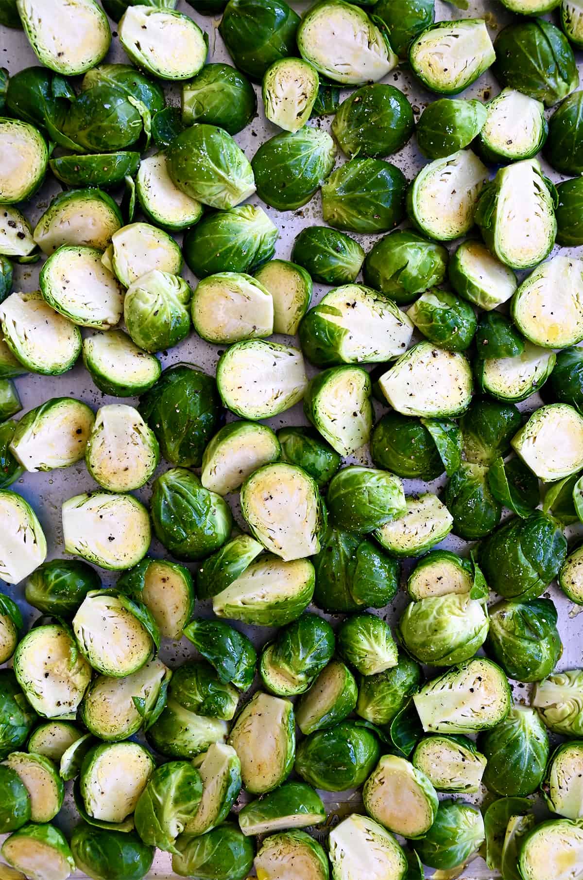 Halved Brussels sprouts coated in olive oil and sprinkled with salt and pepper on a baking sheet.