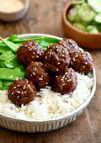 Blackberry jam meatballs garnished with sesame seeds atop white rice in a bowl with snap peas.