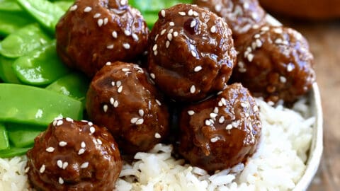 Blackberry jam meatballs garnished with sesame seeds atop white rice in a bowl with snap peas.