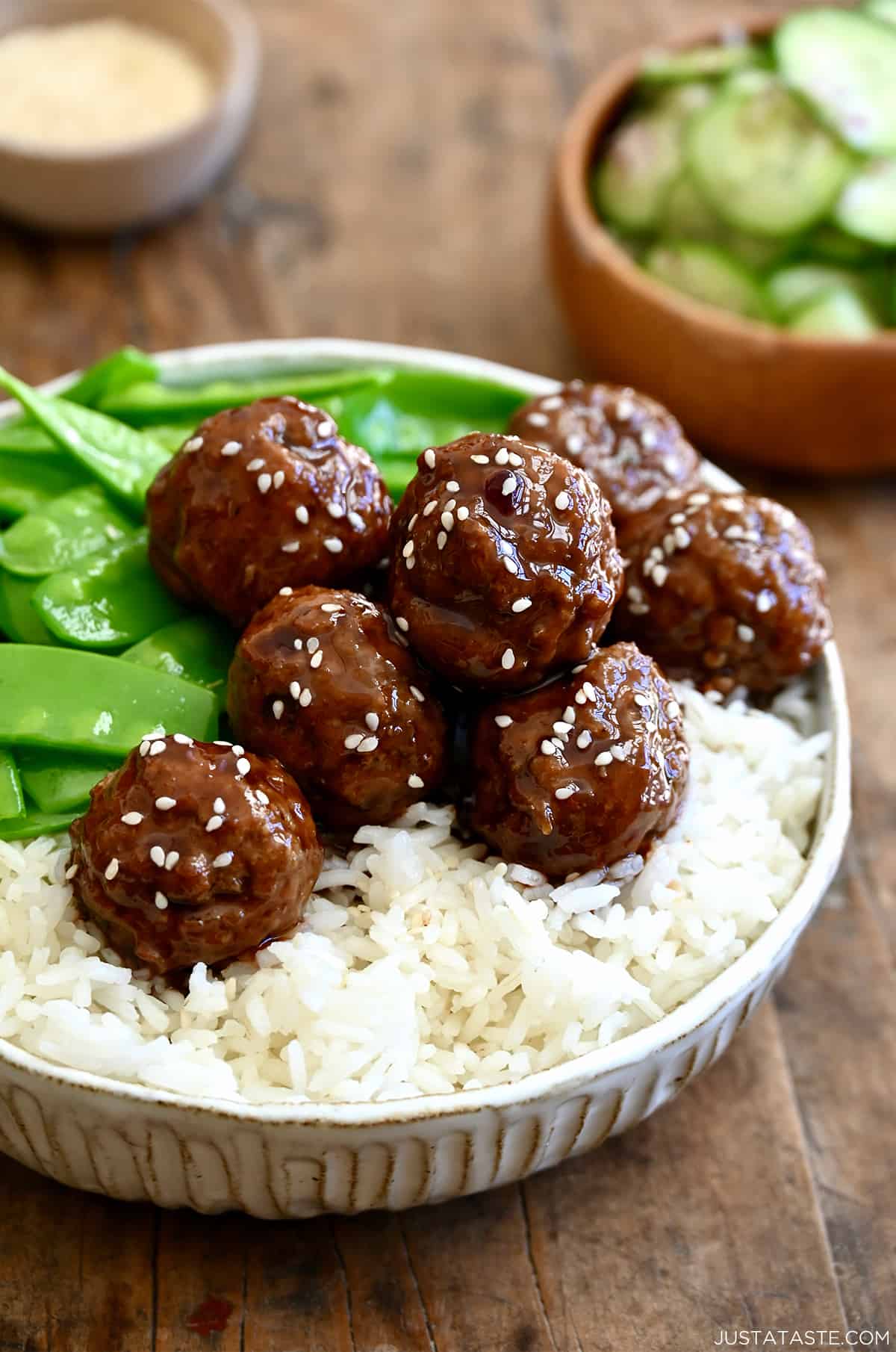 Blackberry jam meatballs garnished with sesame seeds atop white rice in a bowl with snap peas.