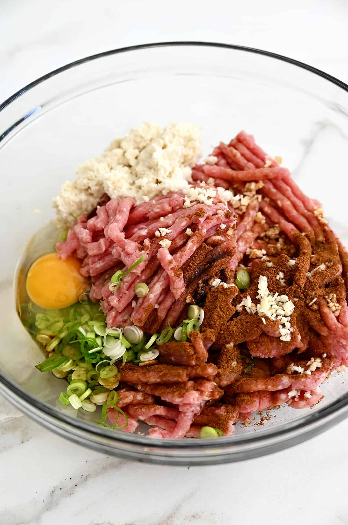 A clear bowl containing ground pork, sliced scallions, an egg, Chinese 5 spice and panko breadcrumbs.