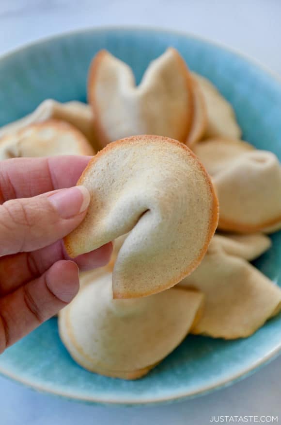 Hand holding Homemade Fortune Cookie with more cookies on a plate in background