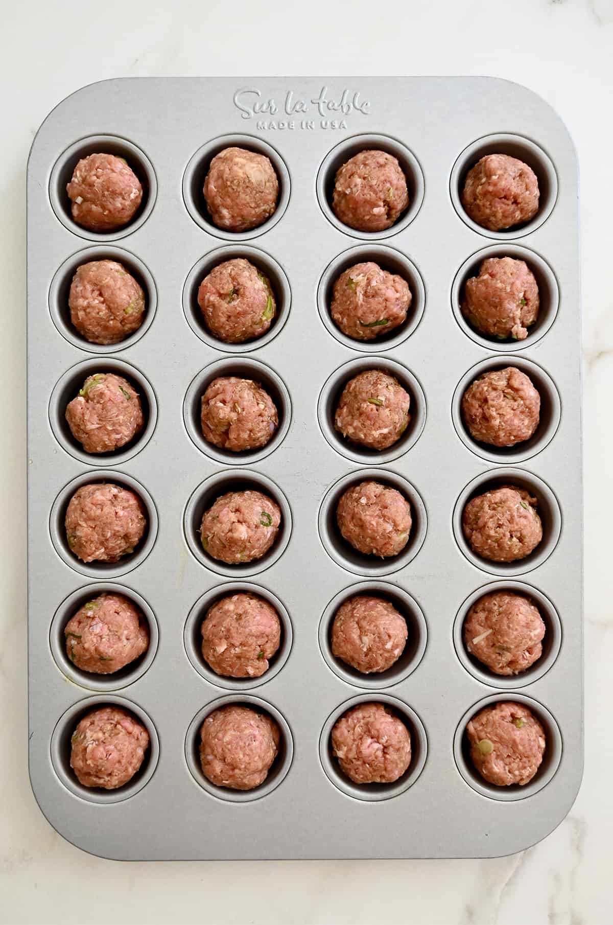 Unbaked meatballs in a mini muffin pan.