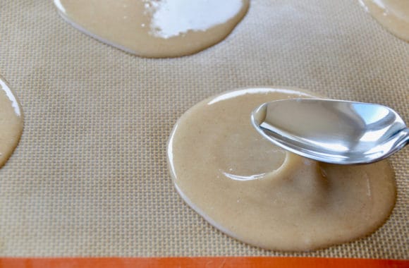 Spoon shaping thin circles of cookie dough on lined baking sheet