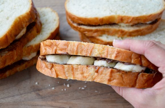 Hand holding two pieces of bread stuffed with Nutella and banana slices