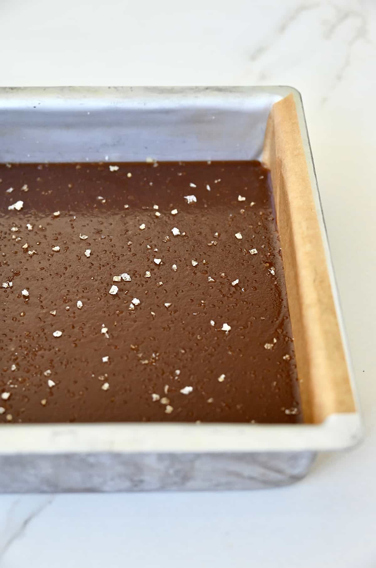 Homemade soft caramels topped with large-flake sea salt in a pan lined with parchment paper.
