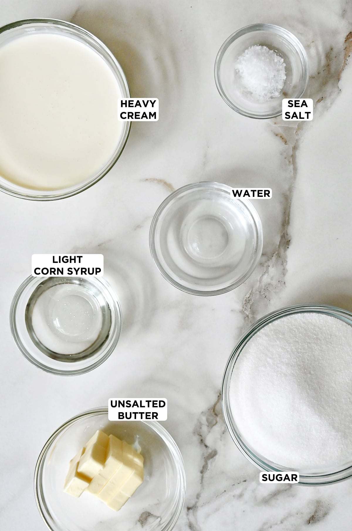 Various sizes of glass bowls containing heavy cream, sea salt, water, sugar, unsalted butter and light corn syrup.